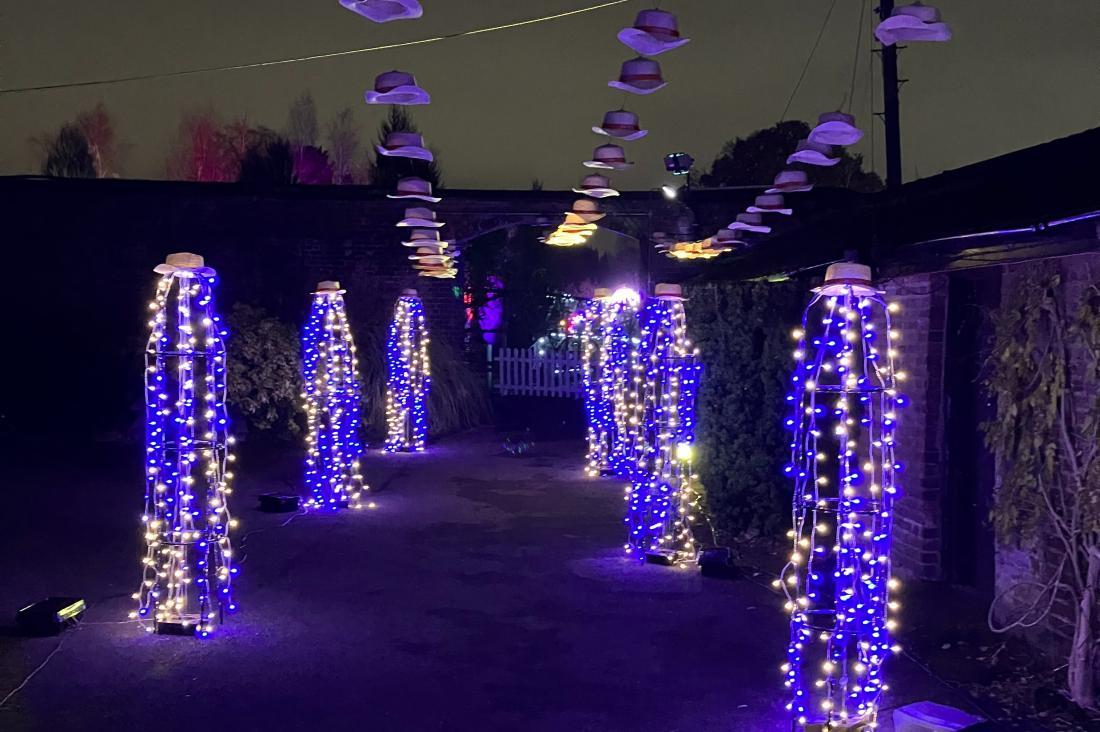 Lit up pathway with straw hats hung around coloured light pillars